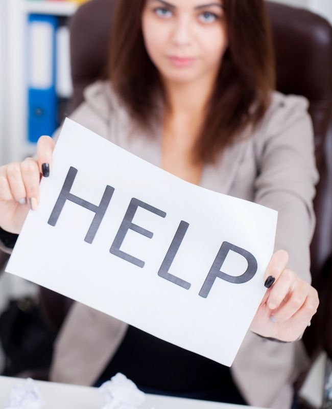 Stressed Business Woman Imploring for Help, Holding a Cardboard with the Message Help . Focus Is on the Cardboard